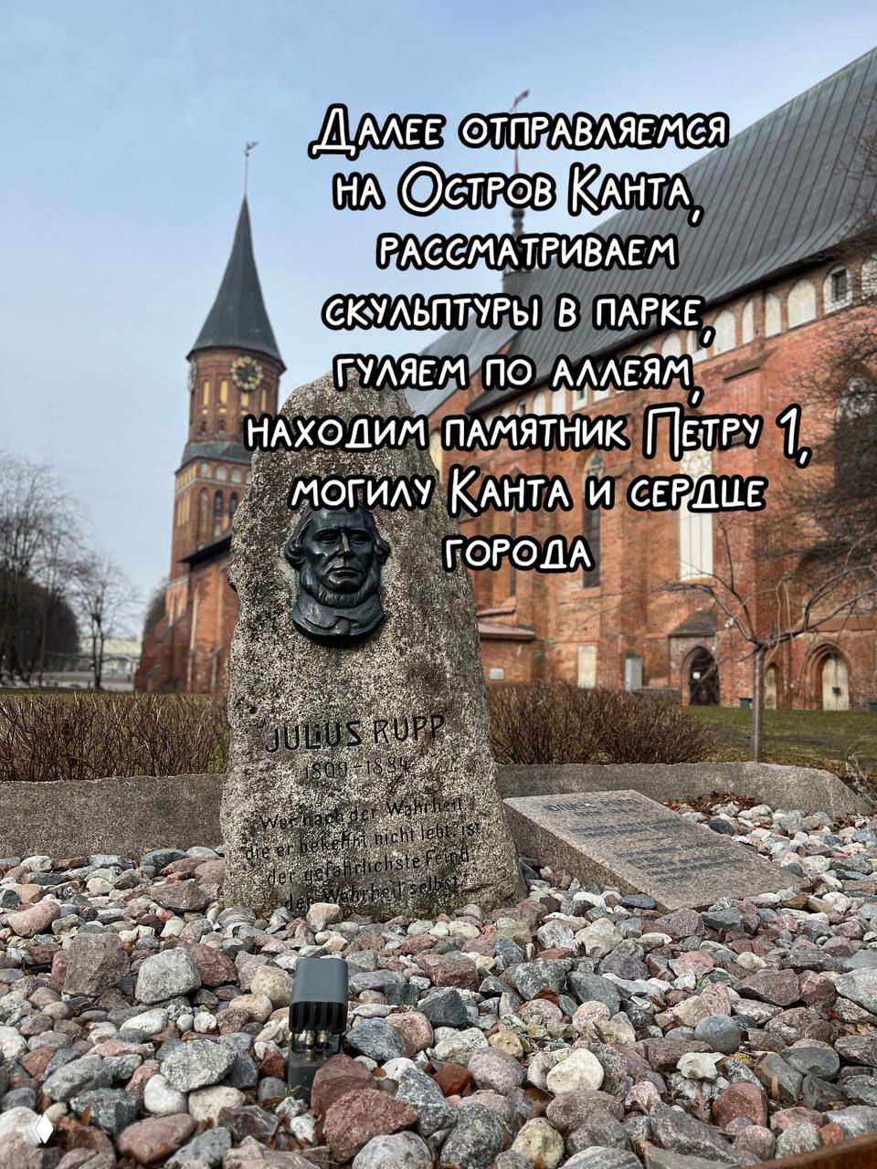 Памятный камень на Острове Канта на фоне Кафедрального собора: бронзовый барельеф, гравировка и отсыпка мелких камней вокруг.