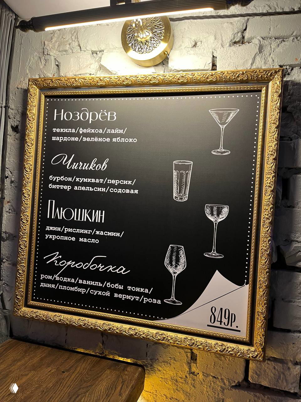 Чёрная меловая доска в золотой рамке с названиями коктейлей (Ноздрёв, Чичиков, Плюшкин и пр.), иллюстрациями бокалов и ценником в рублях на фоне стены бара.