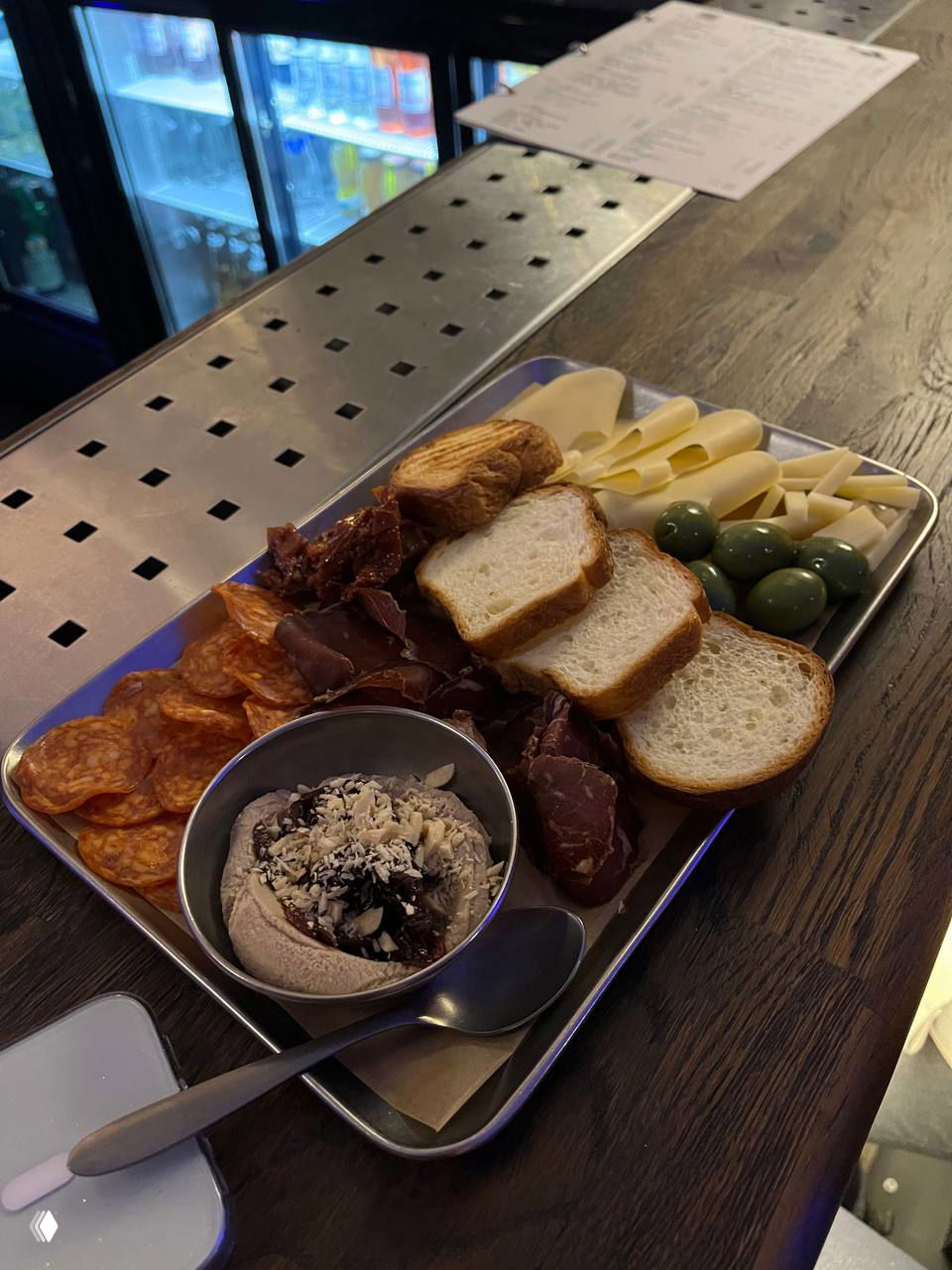 Поднос с закусками: ломтики хлеба, сыры, оливки, вяленое мясо и паста — порция для компании, поданная как закуска к напиткам в баре.