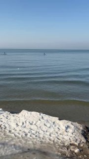 Морской пейзаж в Зеленоградске ранней весной: спокойная Балтийская гладь, снежный берег и чистое голубое небо.