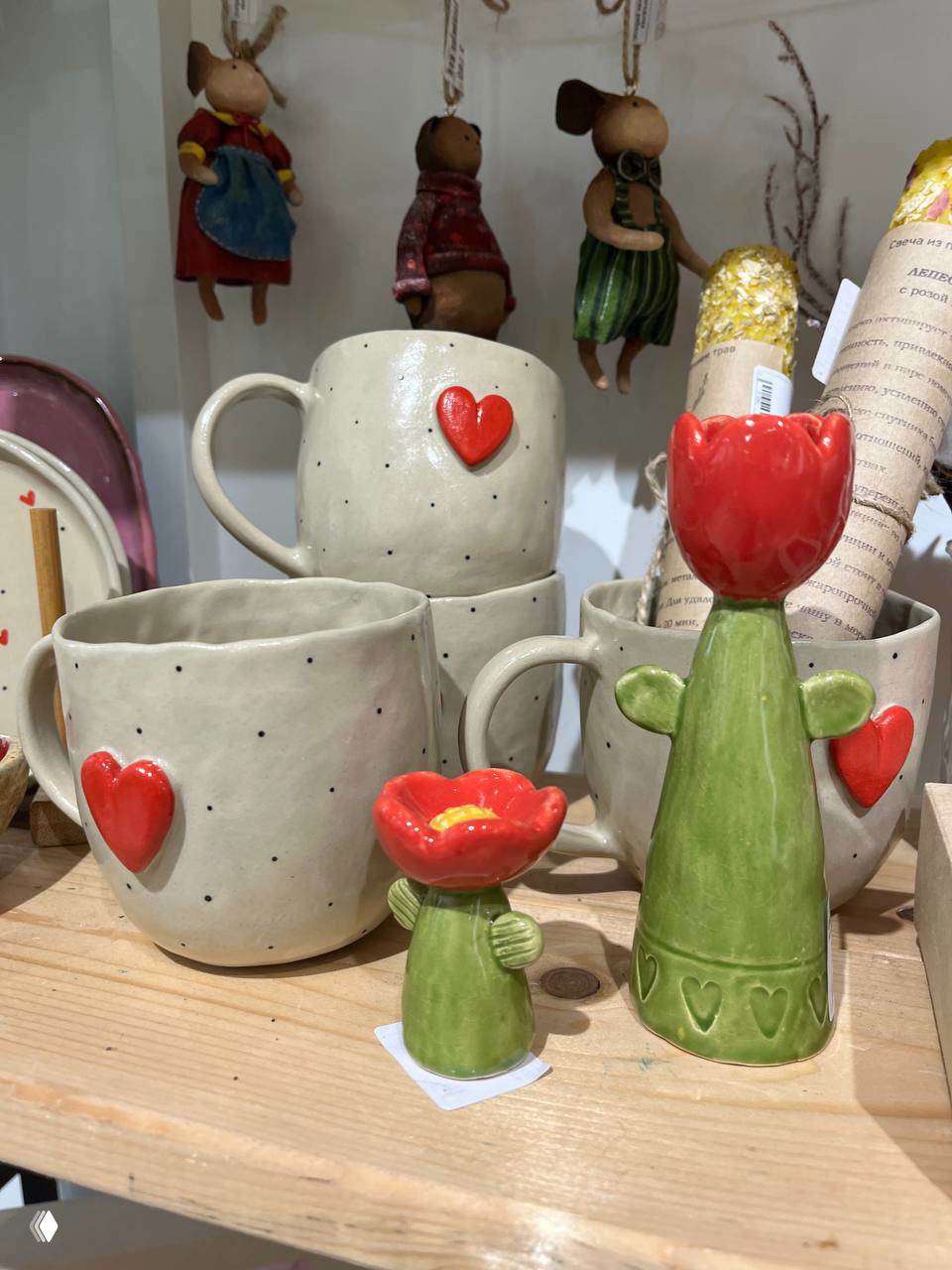 Крупный план керамических чашек с красными сердечками и маленькими декоративными фигурками — предметы ручной работы на полке магазина
