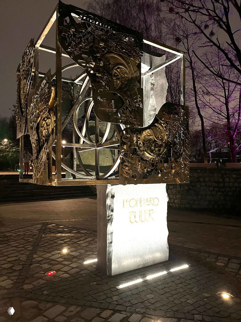 Ночная фотография металлической кубической скульптуры с орнаментными панелями, расположенной на постаменте возле северной набережной острова Канта в Калининграде.