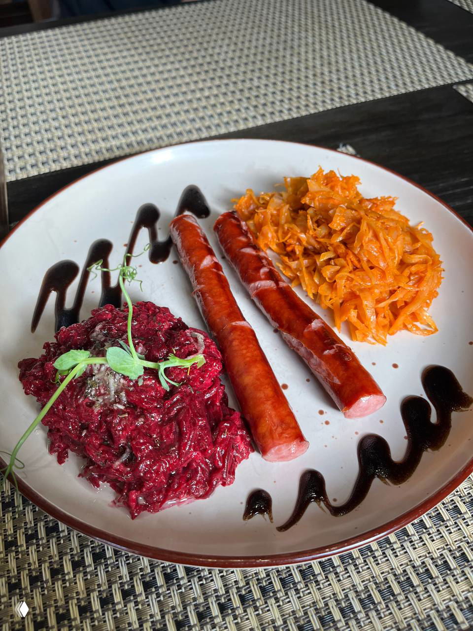 Блюдо с двумя жареными колбасками, свекольным и морковным салатами и декоративными полосами соуса — в кафе в Железнодорожном районе.