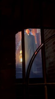 Кадр через окно на фигуру в старинном костюме на лестнице — сценка из квест-экскурсии в замке Тапиау, подсветка и атмосфера.