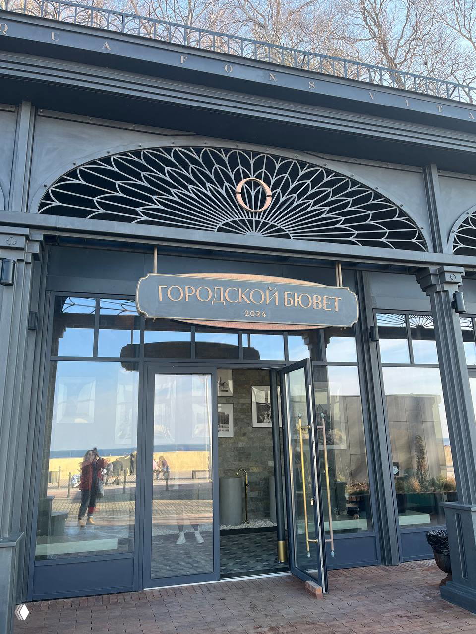Фасад городского бювета в Светлогорске у моря: вход с дверями и вывеской «Городской бювет», виден променад и морской берег рядом.