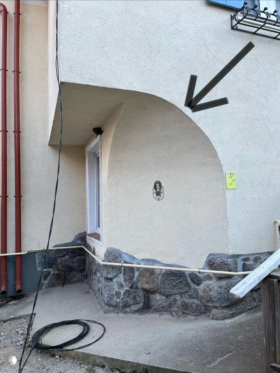 Угол жилого дома в Калининграде с округлым скосом фасада над входом, каменным цокольом и свернутым кабелем у пола.