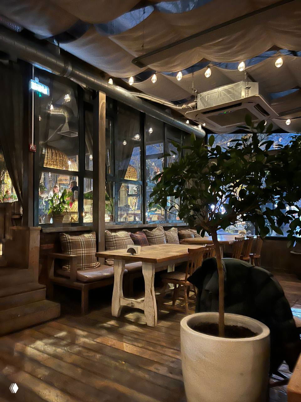 Большие окна, плетёные светильники и уютные скамьи в дальней зоне зала — посадочные места с пледами и мягкими подушками для семейных ужинов.