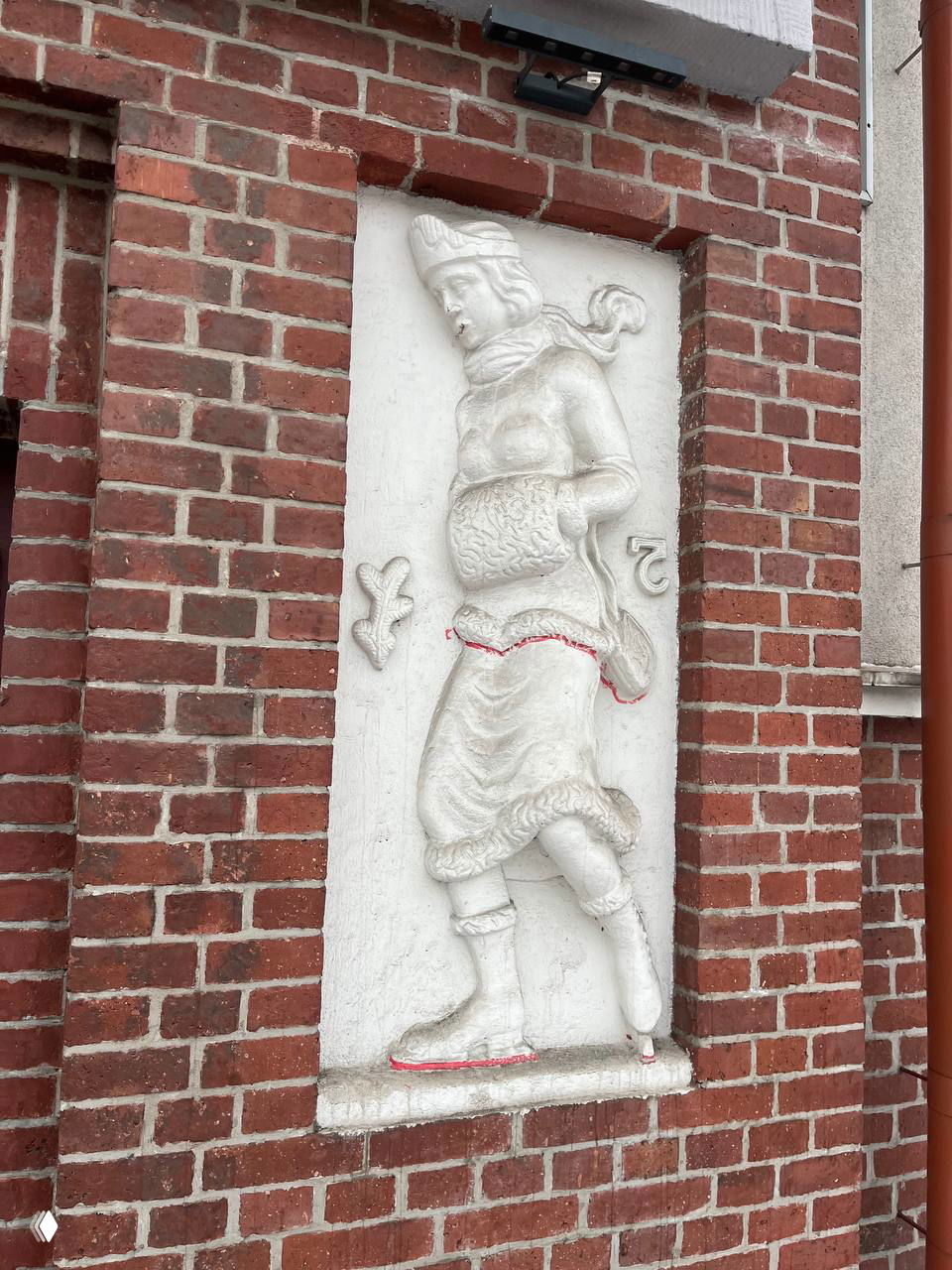 Барельеф мужского образа с рогом изобилия и элементами земледельческой символики; белая скульптура в нише на красной кирпичной стене.