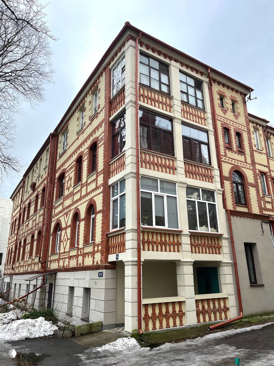 Угловой многоквартирный дом с декоративной красно‑белой кирпичной кладкой и застеклёнными балконами на Комсомольской; фасад с орнаментом и окнами.