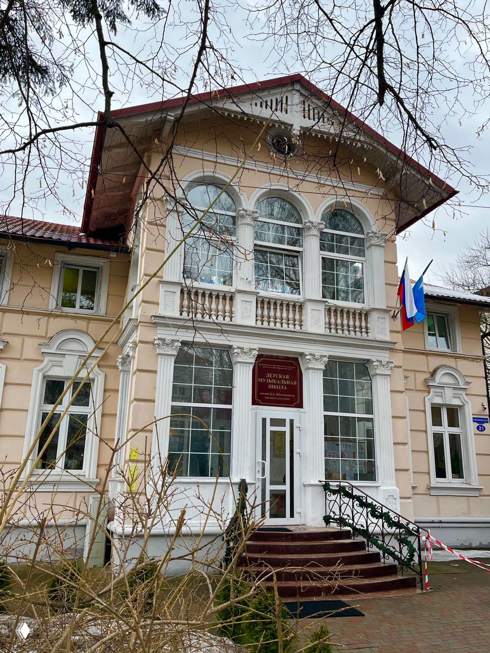 Светлая вилла с большой лоджией, колоннами и балюстрадой, у входа висят флаги — здание общественного назначения на улице Комсомольской в Калининграде.