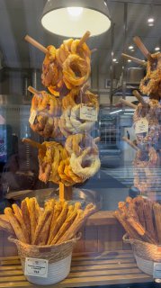 Фотография витрины пекарни на курорте: крендели разных форм и вкусов развешены на стойках, корзины с хлебными палочками.