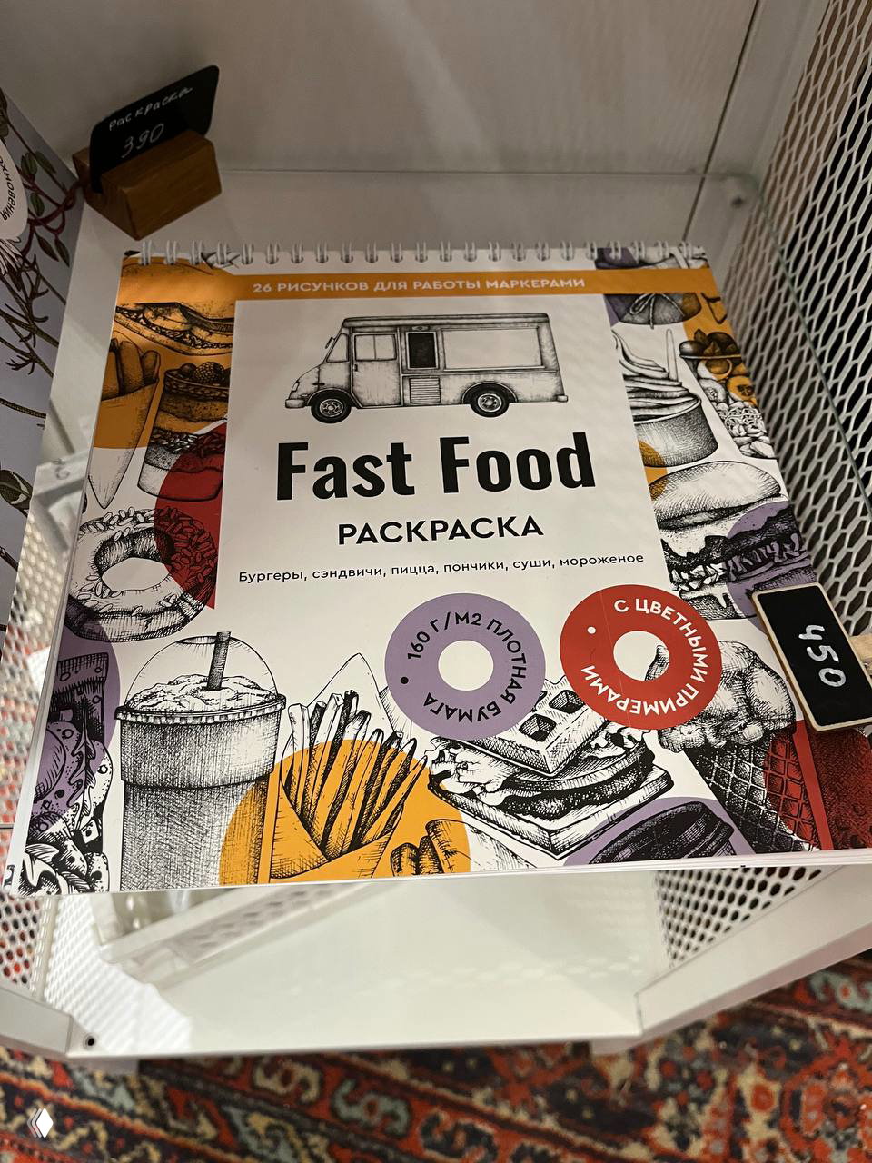 Полка с раскраской «Fast Food» и ценниками в мини-магазине при кафе — товары и сувениры, выставленные для продажи внутри заведения.