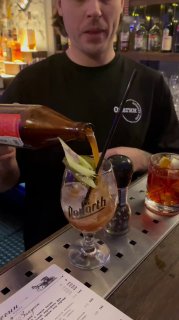 Бармен льёт коктейль в бокал: видны руки, лёд и гарнир, процесс приготовления на баре в вечерней атмосфере одного из калининградских баров.