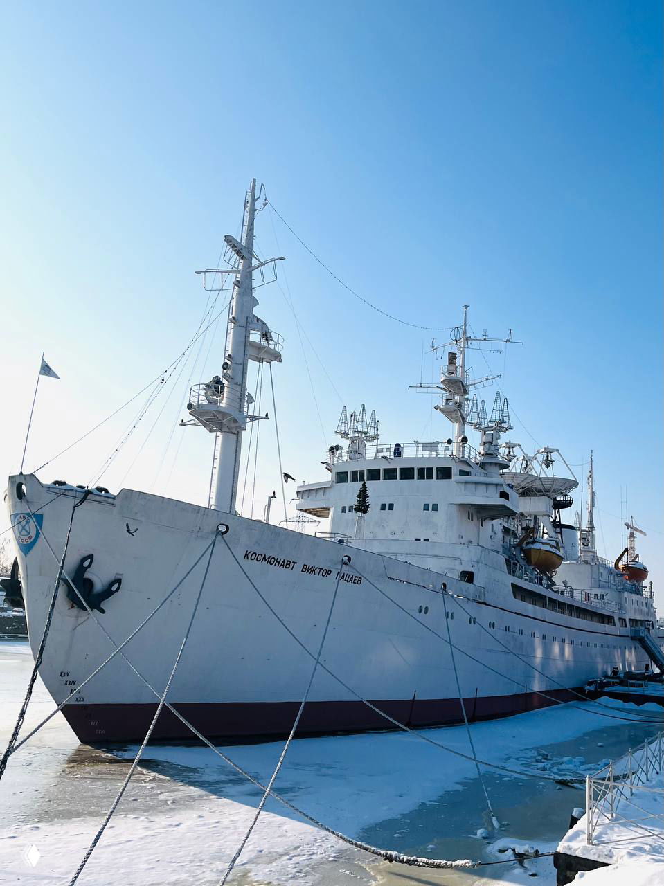Причал с кораблём «Космонавт Виктор Пацаев»: нос судна, тросы и частично замёрзшая вода у пирса в ясный зимний день.