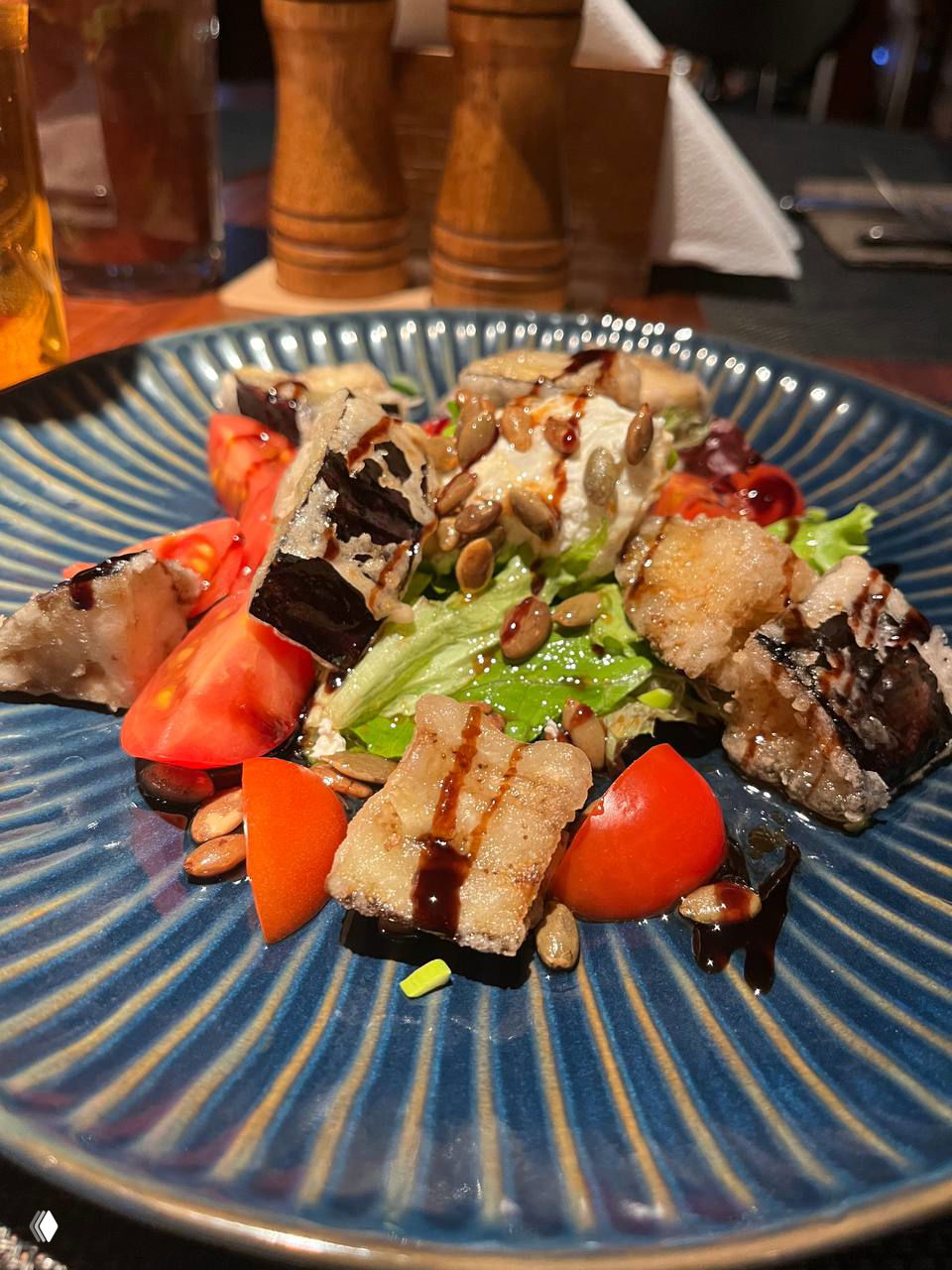 Салат на синей тарелке: свежие томаты, листовой салат, обжаренные кусочки и семена тыквы с бальзамической глазурью — подача в пабе.