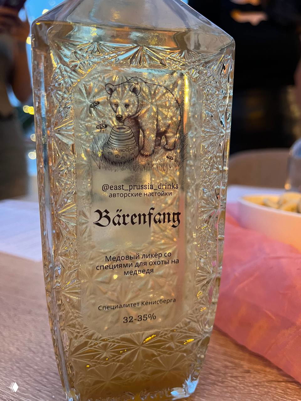 Этикетка бутылки с изображением медведя и надписью Bärenfang; медовый ликёр со специями на столе мастерской, рельеф стекла виден крупно.