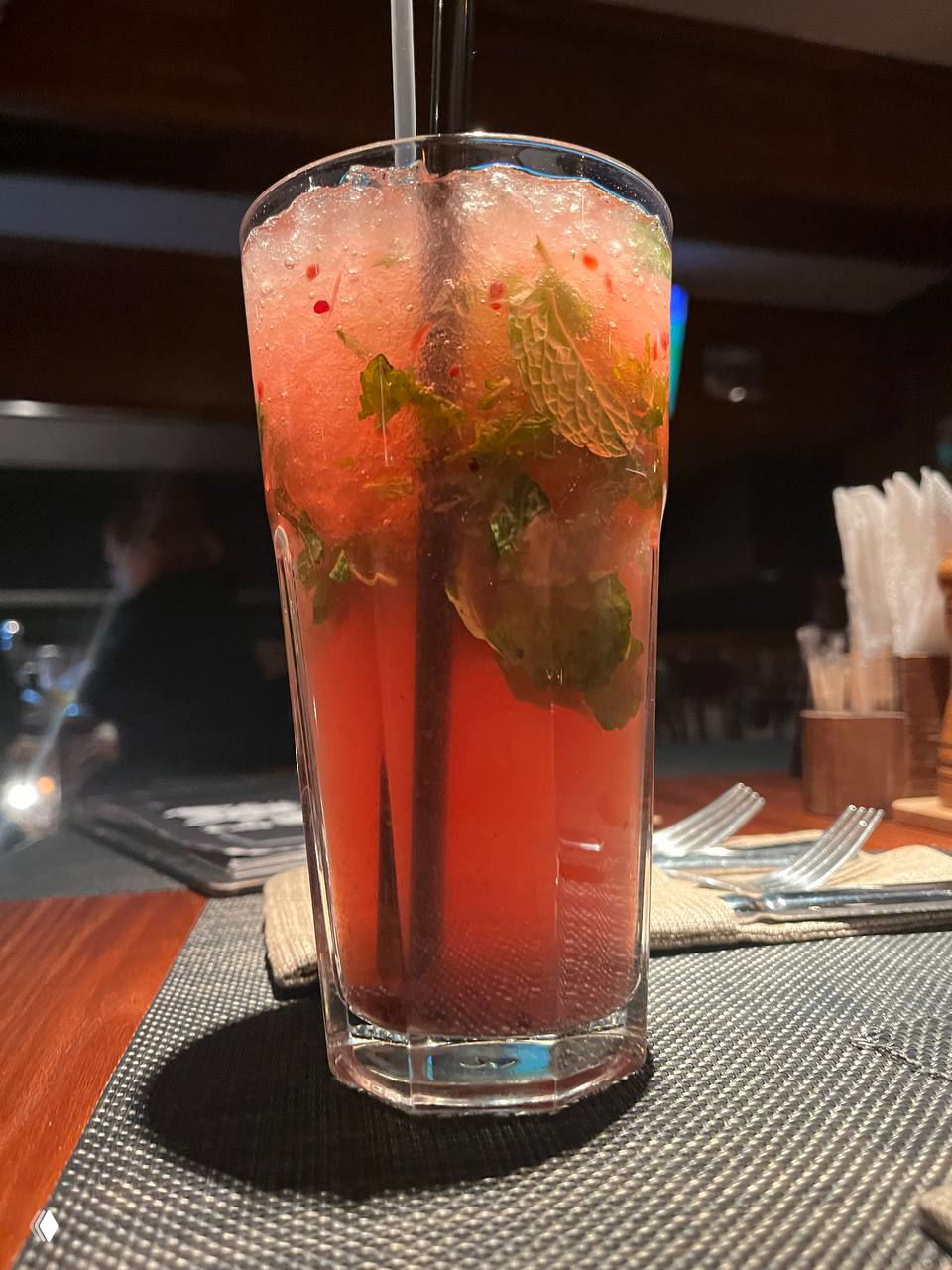 Высокий стакан прохладного яркого коктейля с мятой и дроблёным льдом на столе в пабе — атмосферный безалкогольный или миксованный напиток.