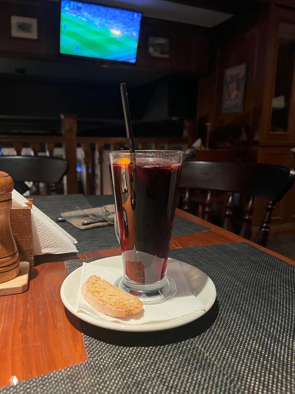 Стакан тёмного горячего напитка с печеньем на маленькой тарелке на фоне деревянного столика и интерьера паба — ночная тёплая атмосфера вечера.