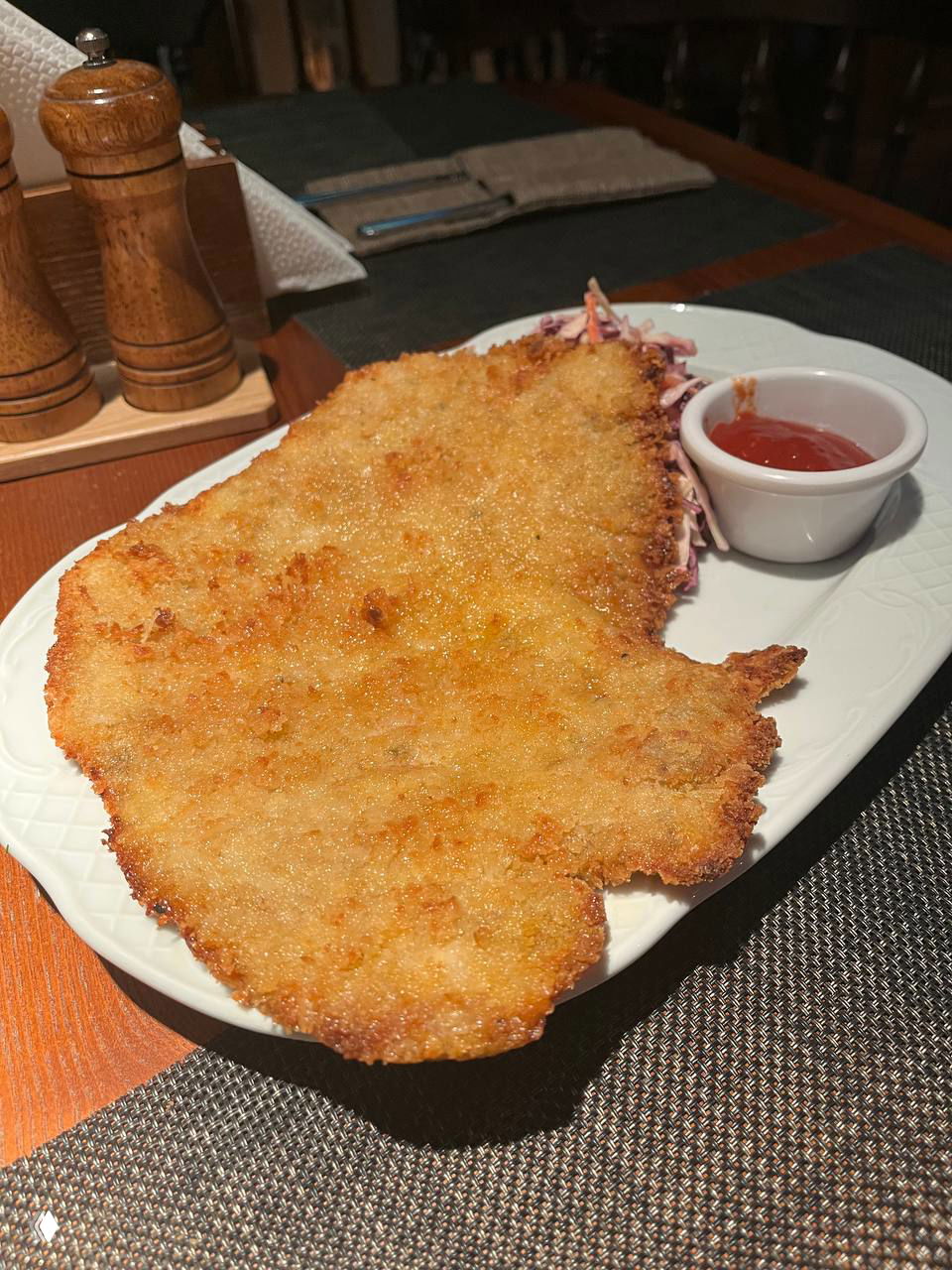 Большой хрустящий шницель на белой овальной тарелке с небольшим соусом-аджикой — классическое сытное блюдо в паб-меню «Британника».