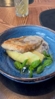 Тарелка с кусочком рыбы на картофельном пюре, покрытой соусом; блюдо подано на синей керамической тарелке в ресторане.