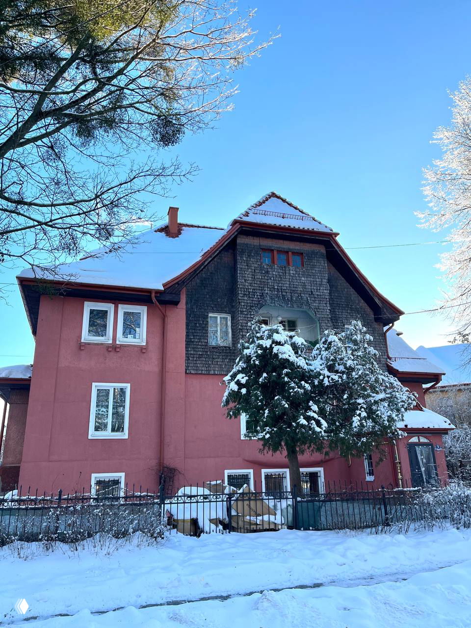 Розово-коричневый фасад старинного дома в Марауненхофе, покрытый снегом: деревянные элементы, забор и небольшое дерево у входа на зимнем фоне.