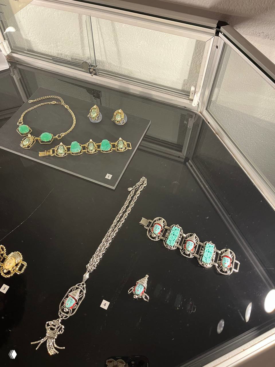 Экспозиция с ожерельем, браслетом и несколькими украшениями с зелёными вставками и миниатюрными камеями на бархатном фоне витрины.