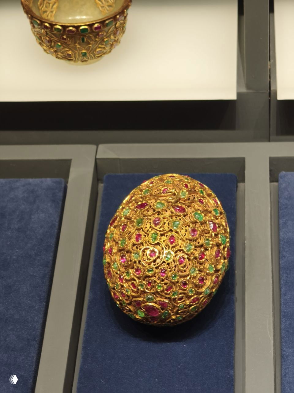 Крупный план овального украшенного яйца Фаберже с золотой филигранью и множеством цветных вставок в музейной экспозиции.