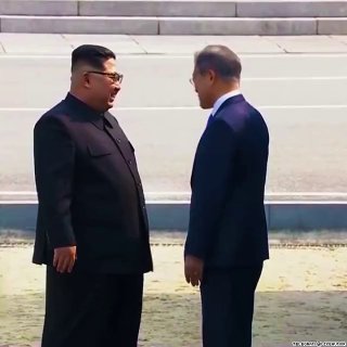 Двое мужчин в официальной одежде беседуют лицом к лицу на открытой церемониальной площадке; кадр показывает их позы и мимику в деловой обстановке.