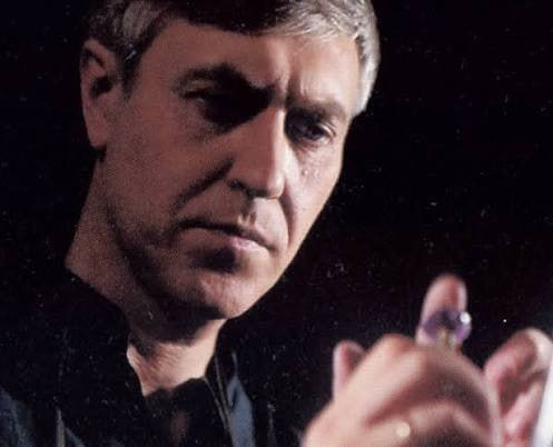 Крупный план мужчины, внимательно рассматривающего небольшой камень в руках; драматичное освещение, сосредоточенный взгляд.