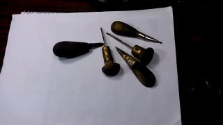 Несколько штихелей с деревянными рукоятками, уложенные на белом листе бумаги на рабочем столе мастера — учебный набор для гравировки.