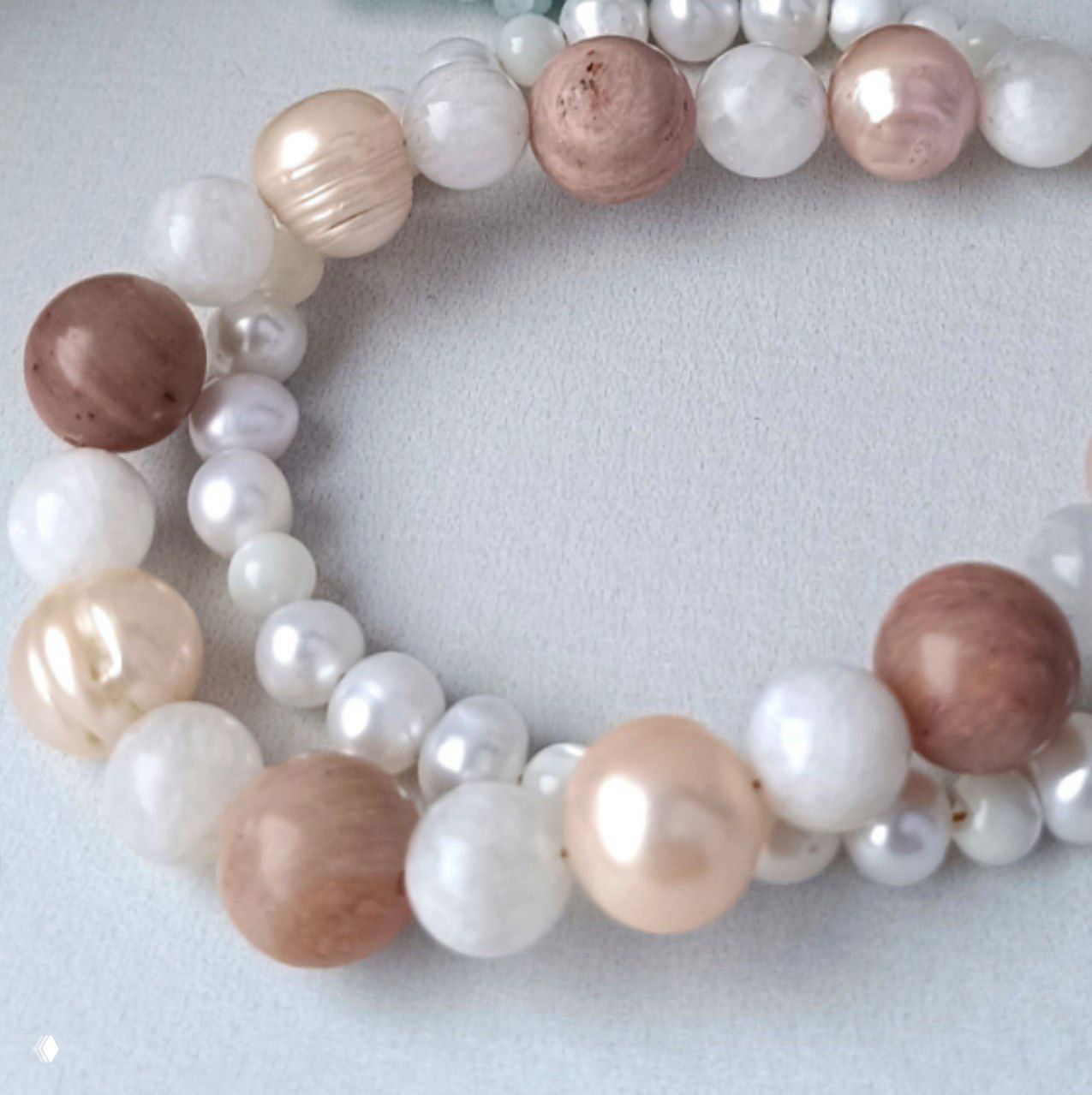 Макросъёмка бус: текстура круглых родонитовых камней, гладкие жемчужины кремового оттенка и белые перламутровые элементы в ансамбле.