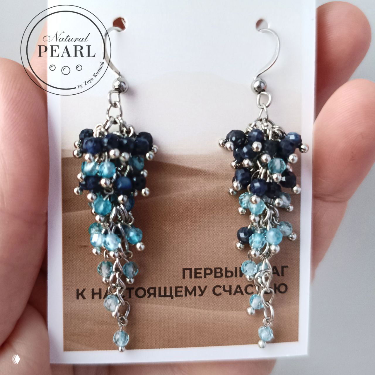 Крупный план пары серёжек‑гроздей: тёмно‑синие сапфиры и голубые топазы, серебристые цепочки и мелкие бусины, студийная съёмка на светлом фоне.