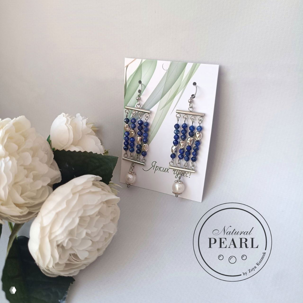 Серьги «Лазуритовый шик» на подставке рядом с белыми декоративными цветами, вид спереди на светлом фоне.