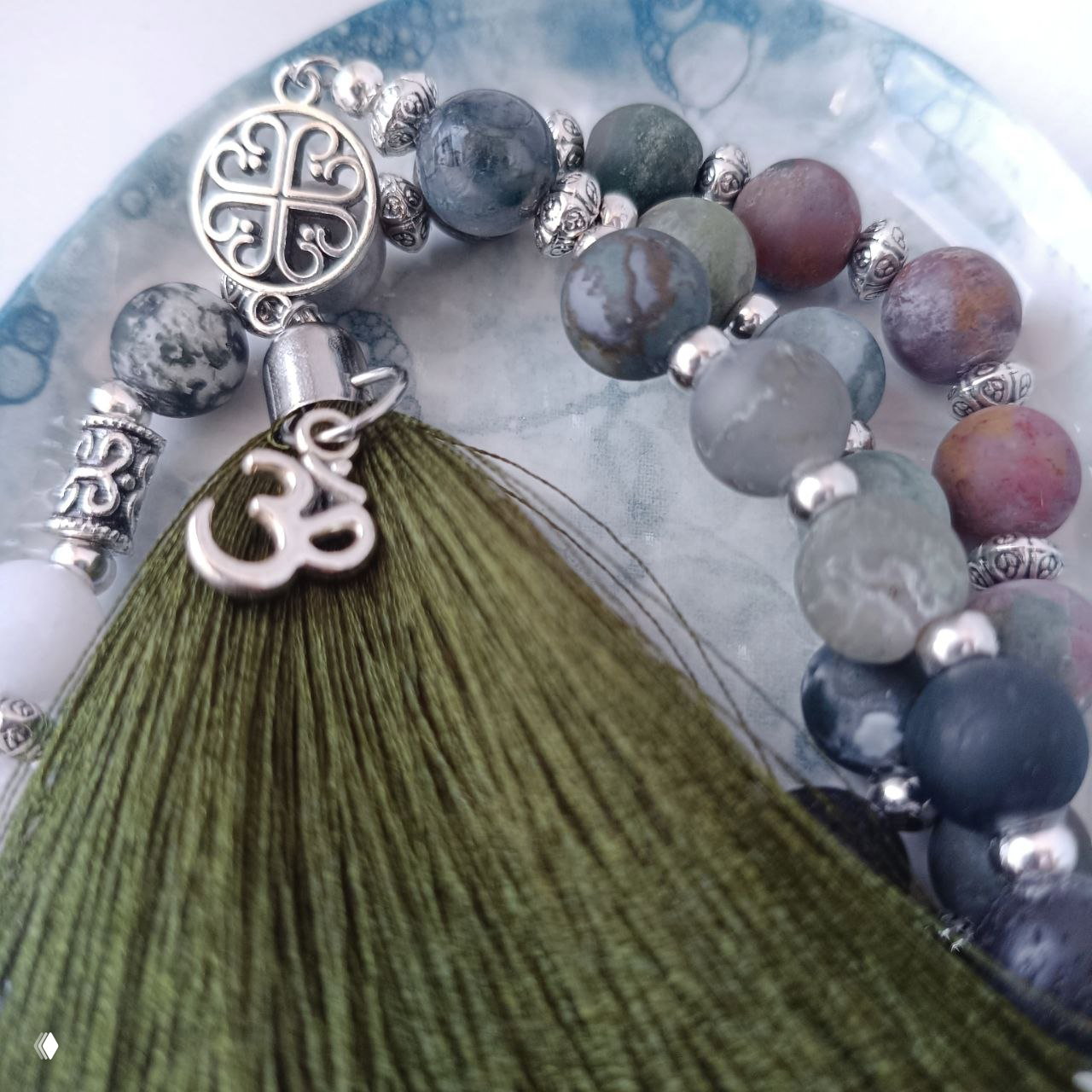 Фрагмент украшений с кистью и круглыми матовыми бусинами яшмы/агата в зелёно-серой гамме и металлическими элементами, показаны текстуры и рисунки камней.