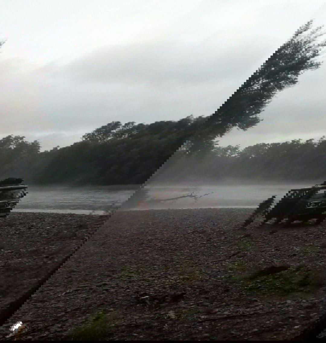 Пейзаж реки и галечный берег с внедорожником у воды; силуэты людей и туман над рекой — кадр из полевой экспедиции, который вдохновляет на украшения.