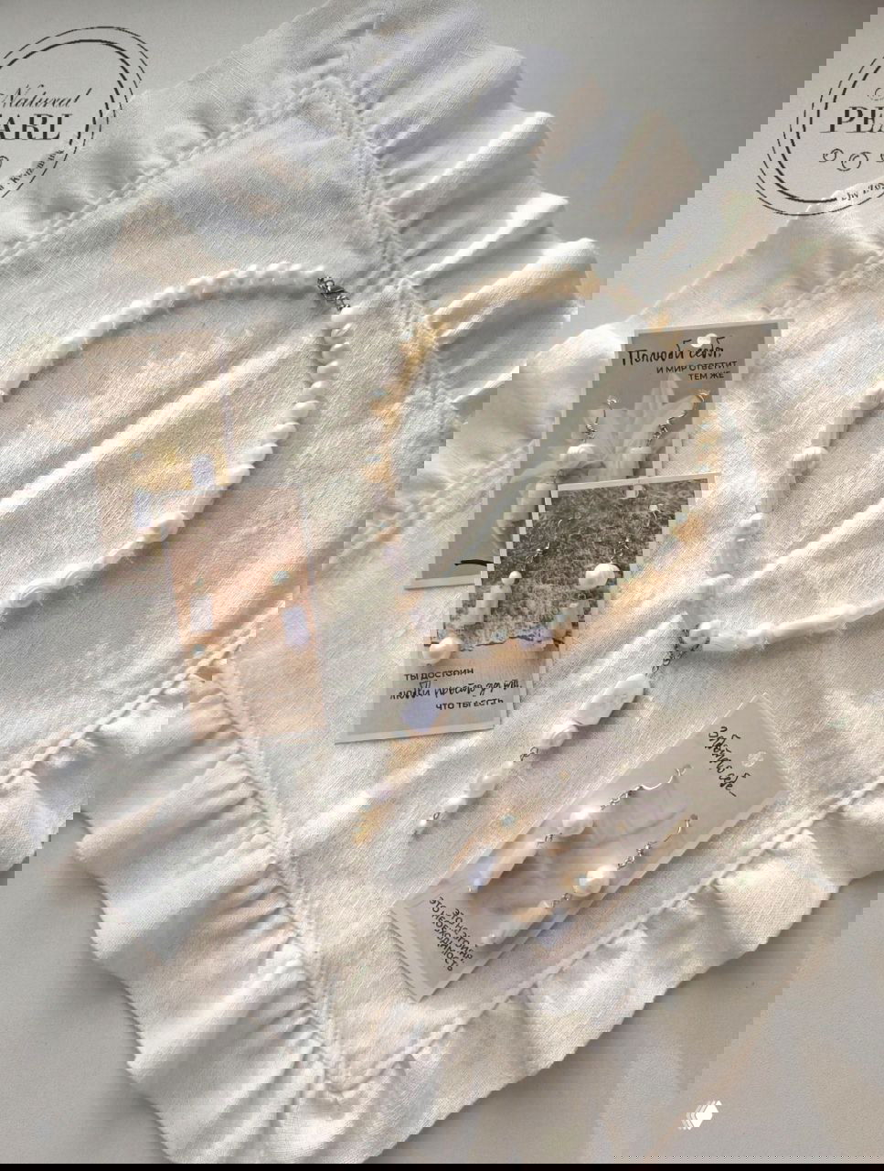 Колье и три пары серёг, выложенные на текстильной салфетке с рюшами — мягкий тёплый свет подчёркивает фактуру жемчуга и перламутра.