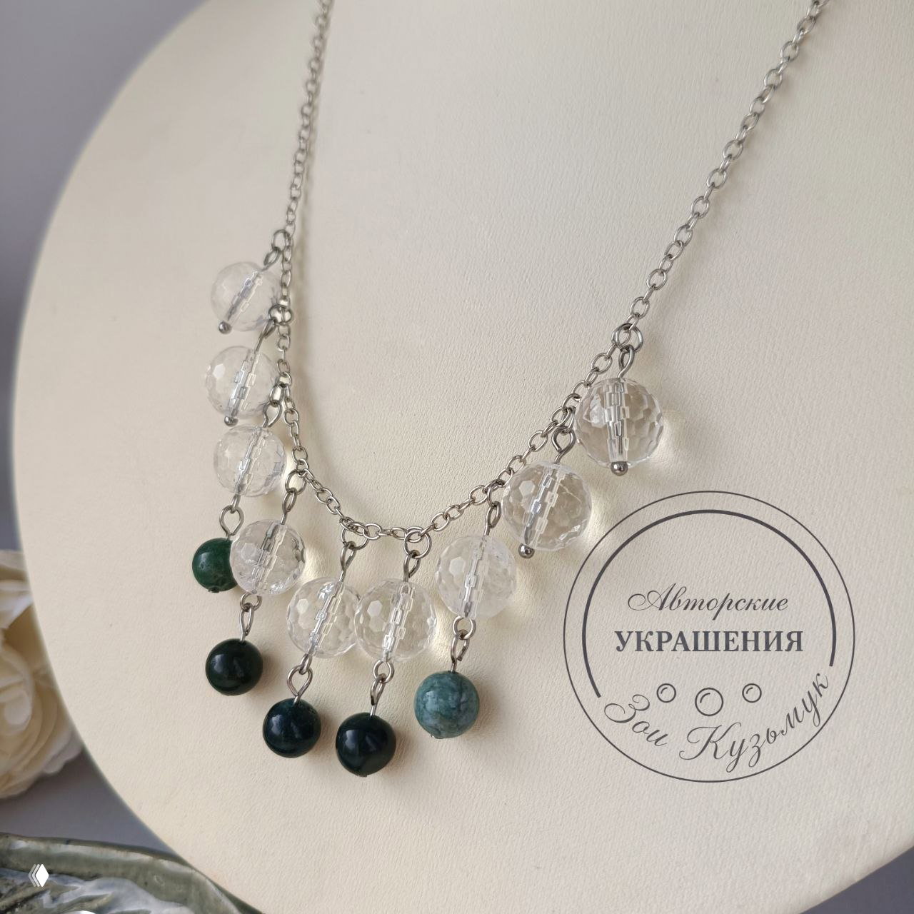 Крупный план цепочки и бусин: прозрачные фасетированные шарики горного хрусталя и зелёные агатовые подвески, виден фирменный штамп автора.