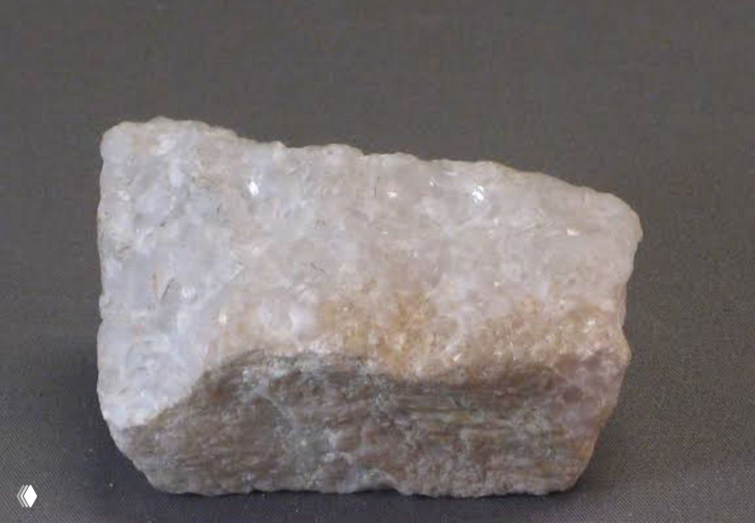 Небольшой образец мрамора на тёмном фоне, видна кристаллическая структура и лёгкий блеск, демонстрирующие текстуру и оттенки камня.