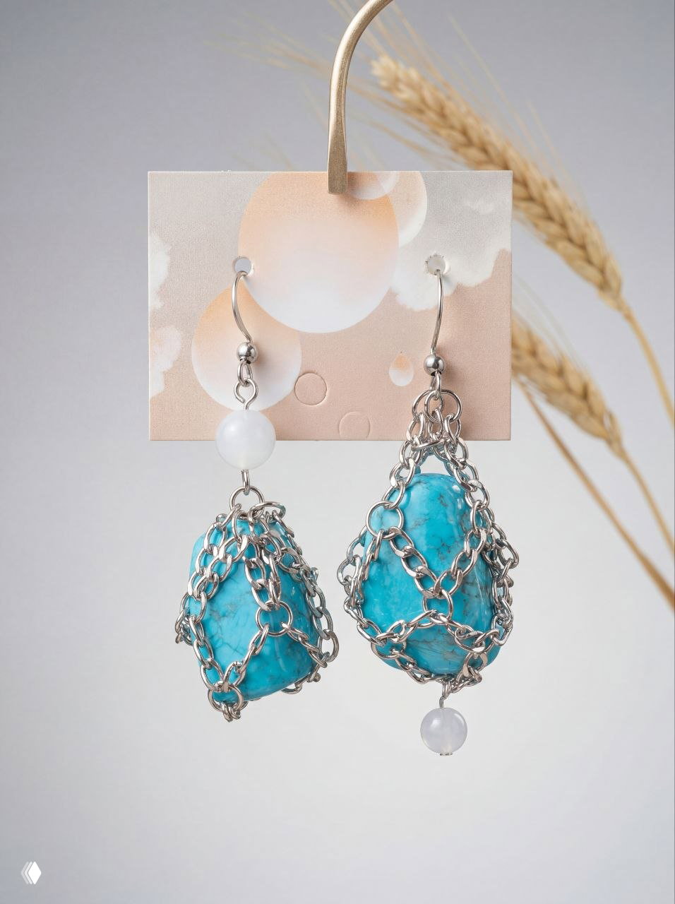 Серьги на карточке: говлитовые бирюзовые камни в металлической цепочной оплётке с белыми бусинами, рядом колосья на светлом фоне.