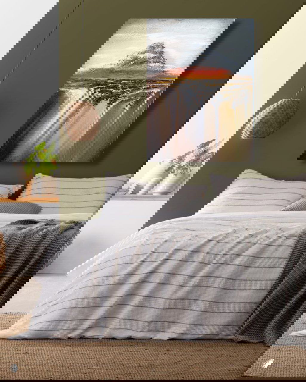 Вертикальная картина с горным сюжетом и текстурой висит над кроватью в уютной спальне с оливковой стеной и лампой в стиле эко, интерьер в спокойных тонах.