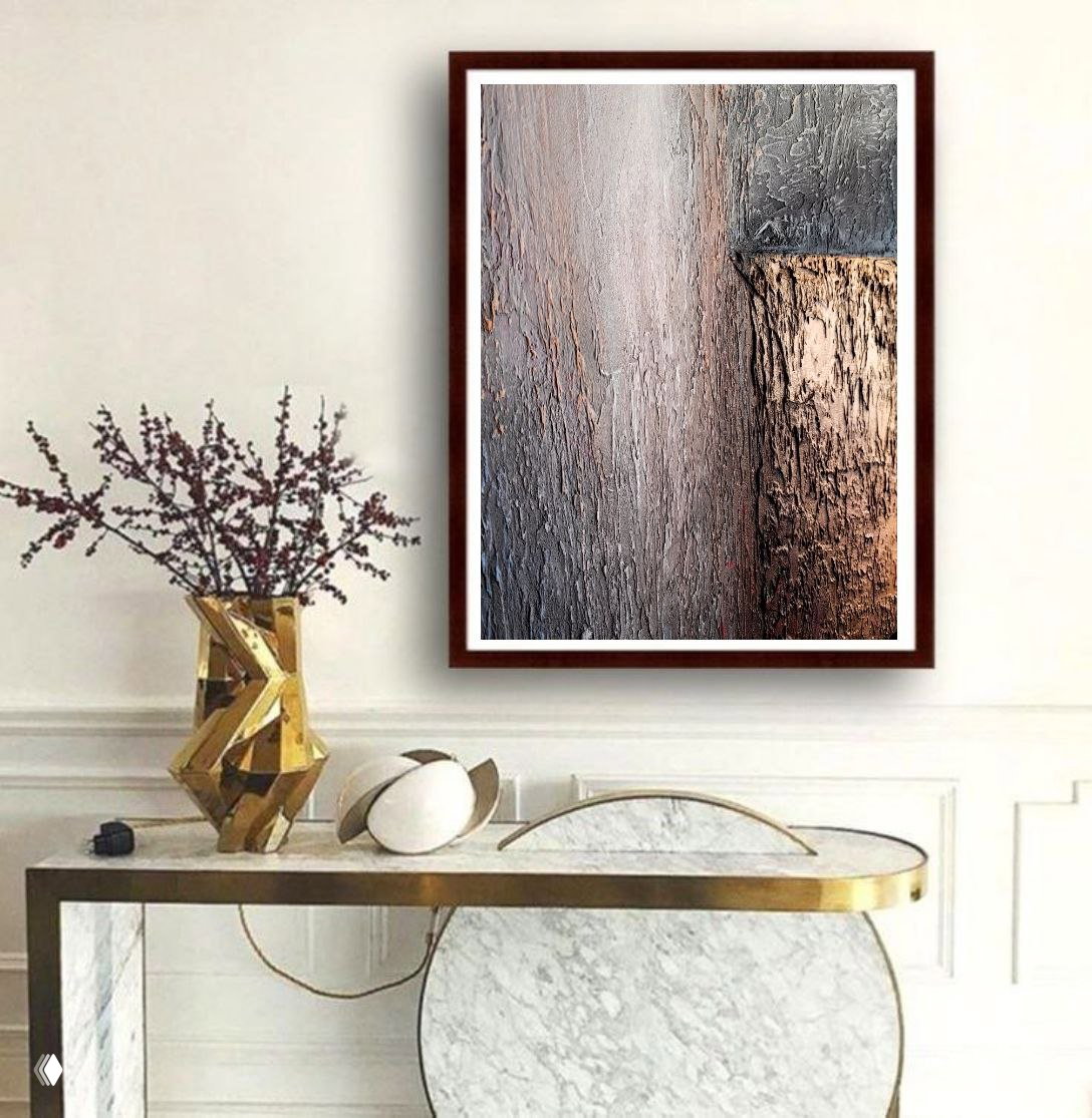 Вертикальная текстурная работа в тёмной рамке висит на светлой стене над консолью с декоративной вазой и золотыми элементами — элегантный классический интерьер.