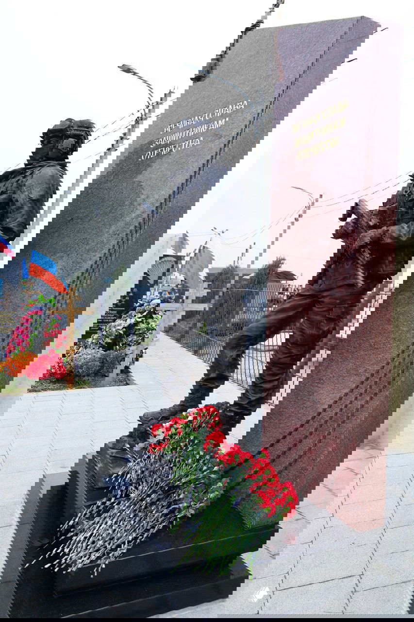 Боковой ракурс памятника «Знамя и честь», цветы у постамента и гранитная стела с надписью «Вечная слава защитникам Отечества».