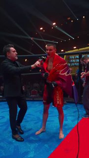 Победитель в центре октагона после боя: Даниил Горшков в красной накидке даёт интервью, рядом ведущий и освещение арены.