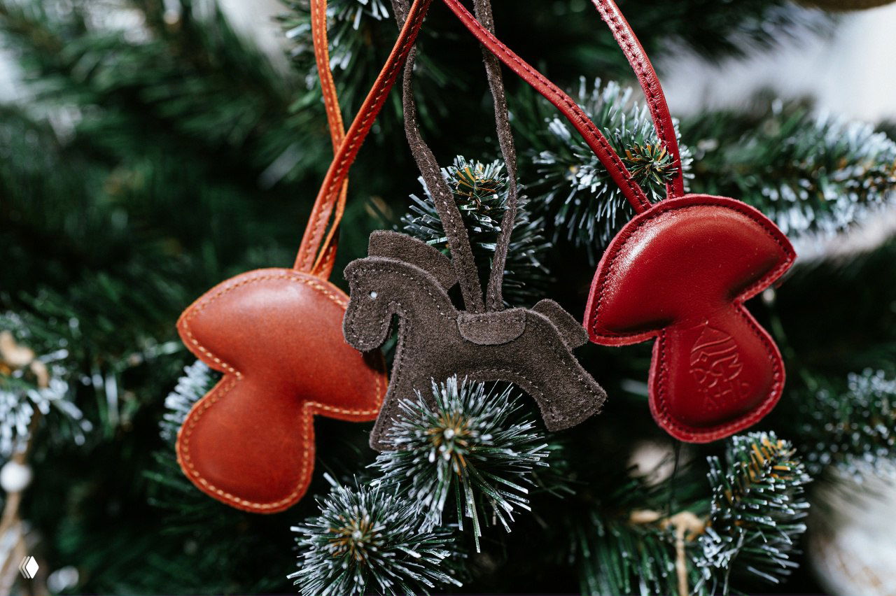 Кожаные сувениры-брелоки в форме лошадки и грибка на ветках елки, видна текстура кожи и рельефный рязанский узор.