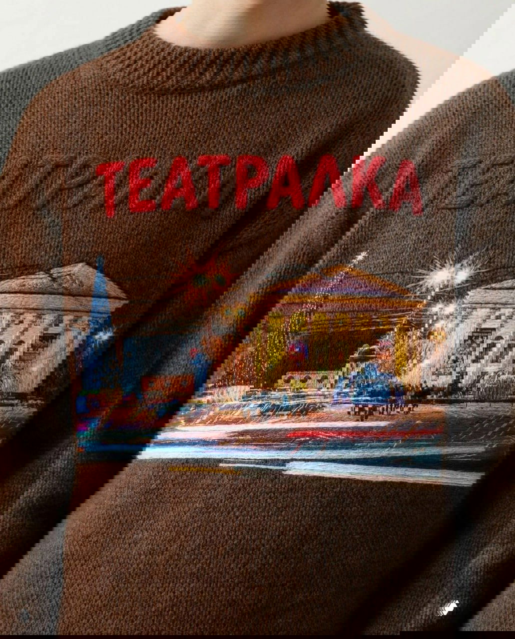 Коричневый свитер с надписью «ТЕАТРАЛКА» и детализированной вышивкой ночного вида на театр с иллюминацией, фонтаном и прохожими на площади.