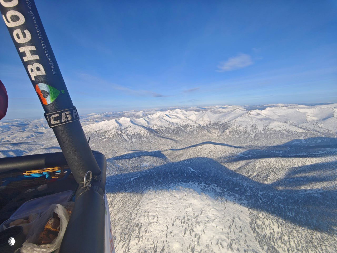 Вид из корзины аэростата на заснеженные горы и леса Хакасии; на раме виден логотип, подчёркивающий перелёт над Кузбассом.