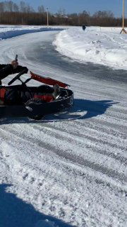 На фото ледовый картинг на заснеженном треке: карт в повороте, снежные валы по краям трассы и зимний пейзаж у озера.