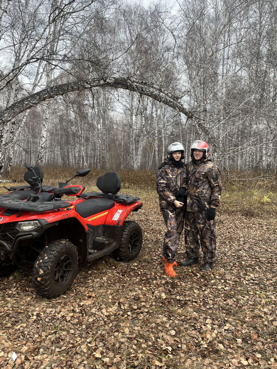 Пара на фоне арки из берёз в лесу рядом с красным квадроциклом, осенние листья на земле; фото для демонстрации живописных остановок на маршрутах проката в Челябинске.