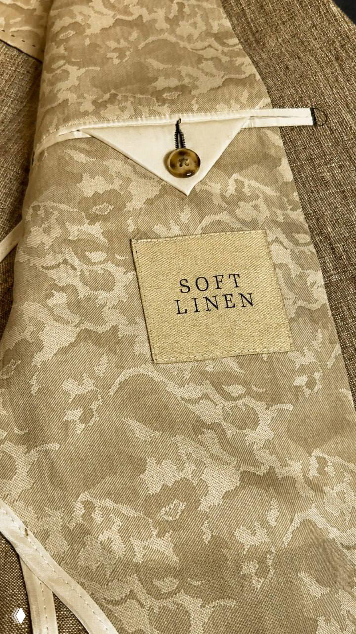 Крупный план нашивки «SOFT LINEN» на жаккардовой подкладке пиджака и фрагмент натуральной льняной структуры ткани рядом с пуговицей.
