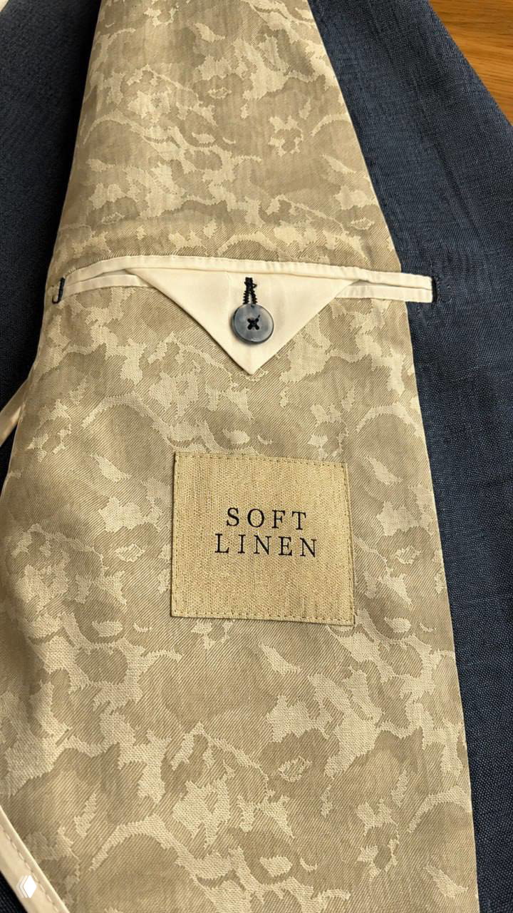 Вид внутренней подкладки пиджака с нашивкой «SOFT LINEN»: бежево-кремовый жаккард и аккуратный карман с пуговицей.